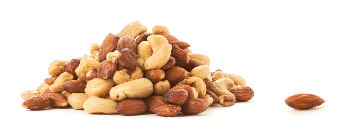 An Almond lying next to a pile of roasted mixed nuts.