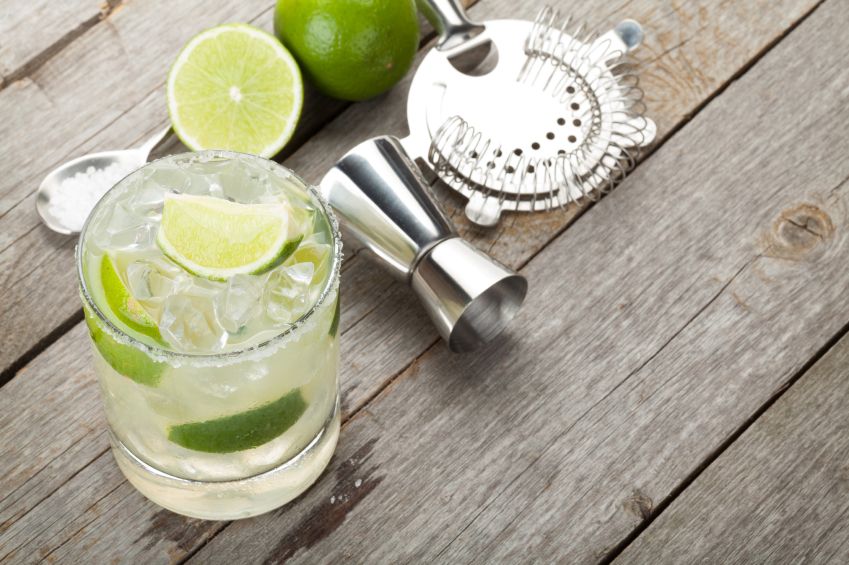 Classic margarita cocktail with salty rim on wooden table with limes and drink utensils