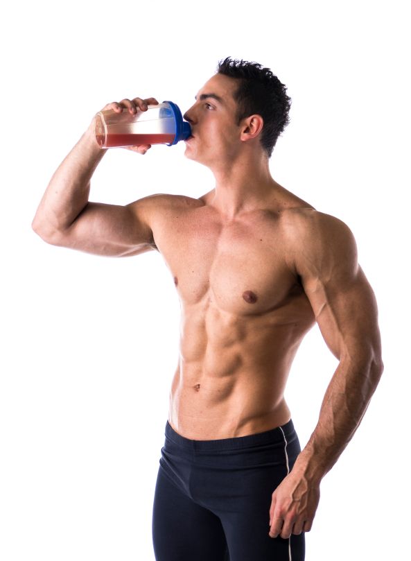 Muscular shirtless male bodybuilder drinking protein shake from blender. Isolated on white, looking at camera