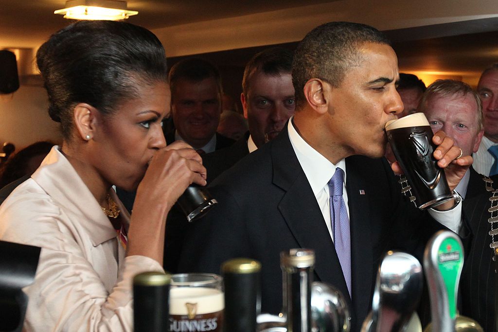 MONEYGALL, IRELAND - MAY 23: U.S. President Barack Obama enjoys a glass of Guinness in his ancestral home of Moneygall alongside First Lady Michelle Obama (L) on May 23, 2011 in Moneygall, Ireland. U.S. President Obama is visiting Ireland for one day at the start of a week long tour of Europe. He will meet with distant relatives in Moneygall and speak at a rally in central Dublin after a concert. (Photo by Irish Government - Pool/Getty Images)