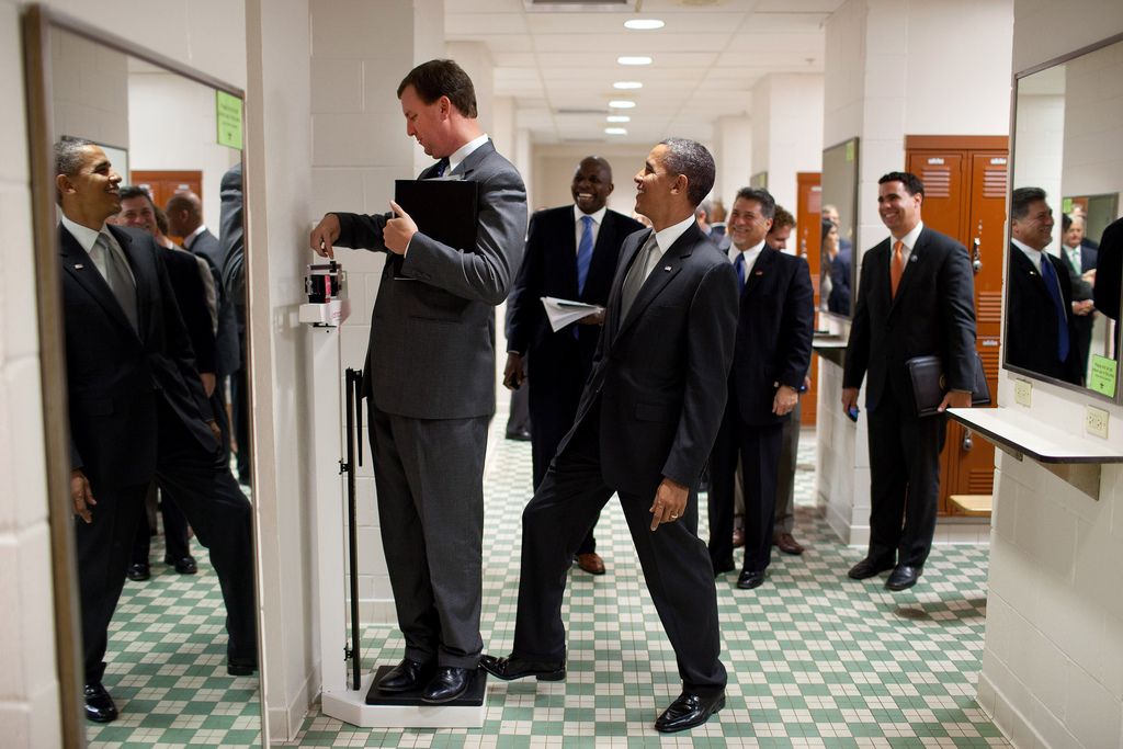 President Barack Obama puts his toe on the scale as Trip Director Marvin Nicholson tries to weigh himself during a hold in the volleyball locker room at the University of Texas in Austin, Texas, Aug. 9, 2010. (Official White House Photo by Pete Souza) This official White House photograph is being made available only for publication by news organizations and/or for personal use printing by the subject(s) of the photograph. The photograph may not be manipulated in any way and may not be used in commercial or political materials, advertisements, emails, products, promotions that in any way suggests approval or endorsement of the President, the First Family, or the White House.