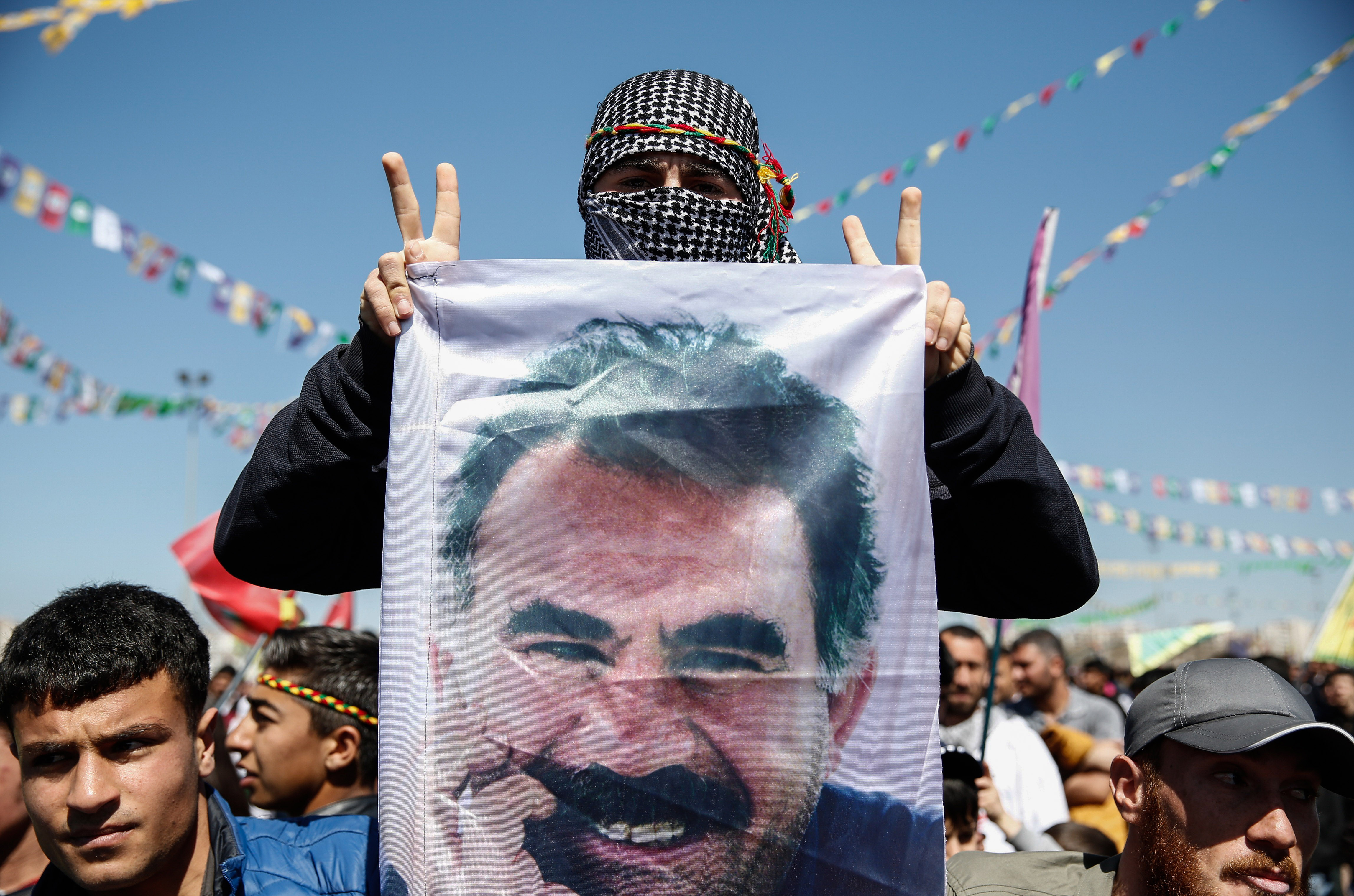 A Kurdish man flashes a v-sign as he holdsup a flag with a picture of the jailed PKK leader Abdullah Ocalan during Newroz celebrations, on March 21, 2015 in Diyarbakir, Turkey. Thousands of Kurds gather for the Newroz spring festival in Diyarbakir in southeast Turkey under tight security after months of fighting between security forces and Kurdish separatists, and a series of bombings in Istanbul and Ankara. (Photo by Ulas Tosun/Getty Images)
