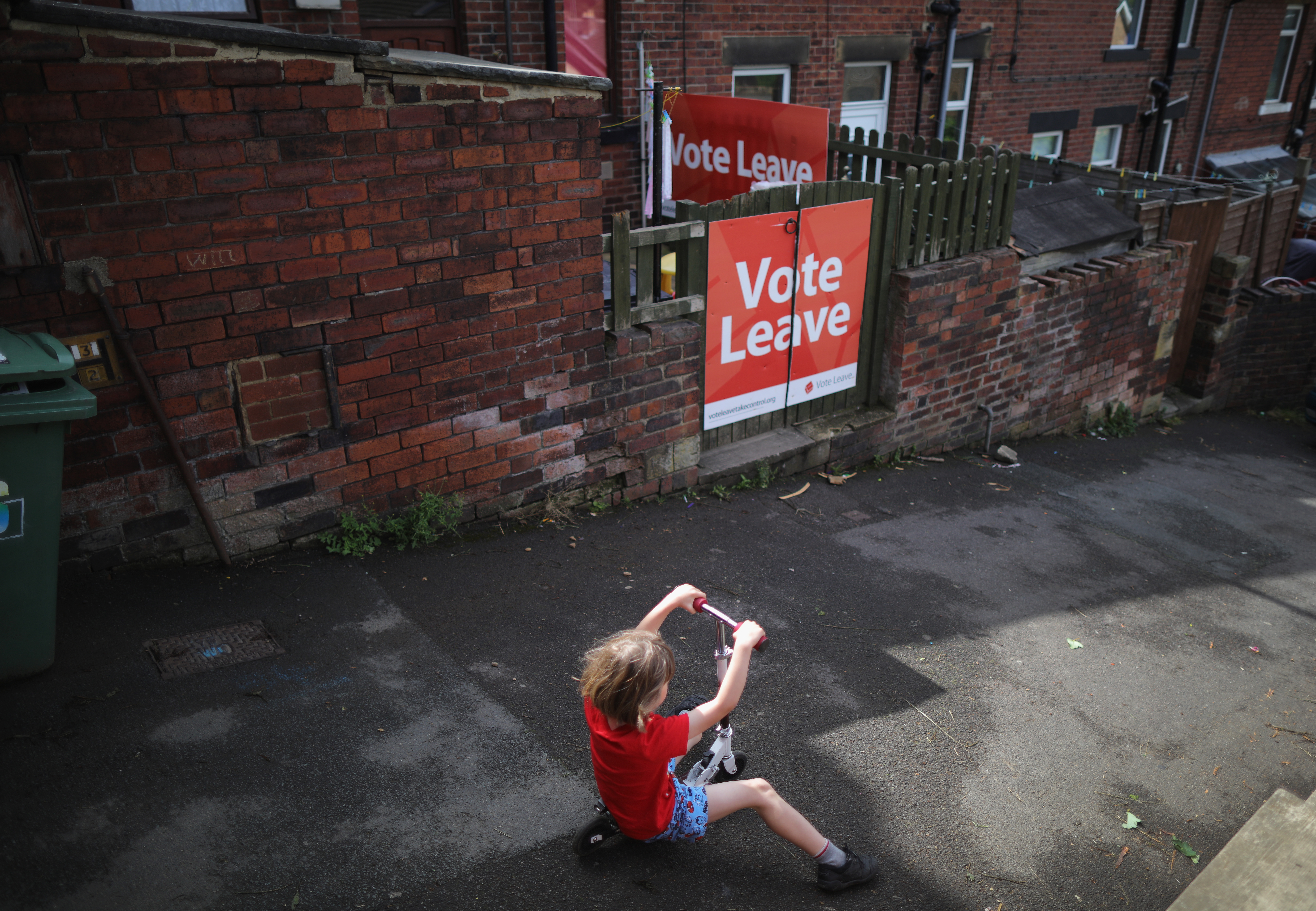 BATLEY, ENGLAND - JUNE 18: A young rides his scooter past a 'Vote Leave' poster in the back alley next to his home in the West Yorkshire town of Batley, in the constituency of murdered MP Jo Cox on June 18, 2016 in Batley, United Kingdom. The Labour MP for Batley and Spen was about to hold her weekly constituency surgery in Birstall Library last Thursday (June 16, 2016) when she was shot and stabbed in the street. (Photo by Christopher Furlong/Getty Images)