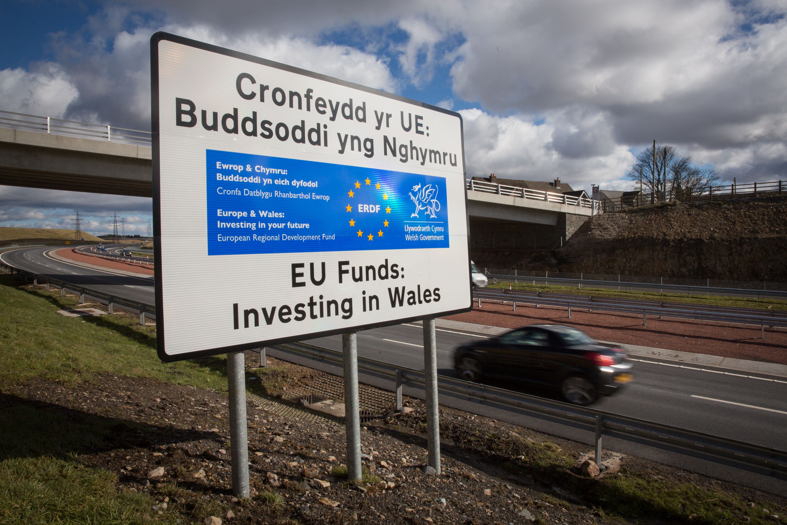 EBBW VALE, UNITED KINGDOM - MARCH 07: A car passes a EU funding sign on the newly opened A465 near Ebbw Vale on March 7, 2016 in Blaenau Gwent, Wales. The West Wales and the Valleys region, which covers 15 local authority areas, has been identified as the poorest region in the whole of north Western Europe, with large swathes of Wales poorer than parts of Bulgaria, Romania and Poland and four-and-a-half times less prosperous than central London, highlighting the fact that the UK now has Europe's highest inequality of wealth within the European Union. To address this, from 2014 to 2020, Wales will benefit from around £1.8bn EU European Structural Funds investment which comprises funding from two separate European Structural Funds: the European Regional Development Fund (ERDF) and the European Social Fund (ESF). The ERDF funds are used for a range of things including urban development, research and innovation, competitiveness, use of renewable energy and energy efficiency, connectivity and urban development. The ESF funds are to be directed to tackling poverty through more sustainable employment, increasing skills and tackling youth unemployment in the region. (Photo by Matt Cardy/Getty Images)