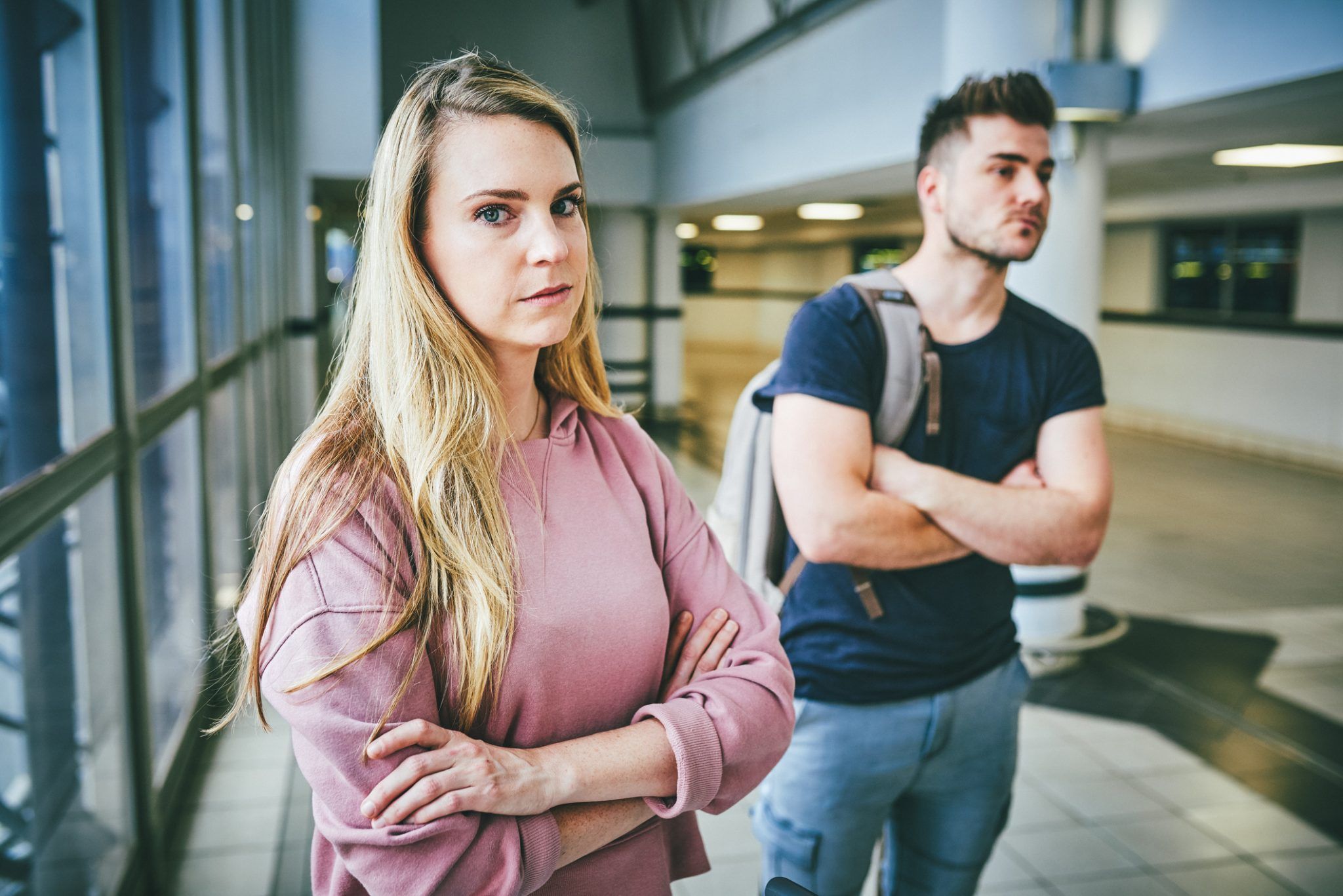 Girlfriend looking unimpressed in airport while boyfriend stands back