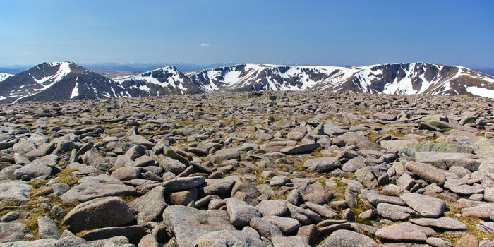 Boulders and rocks on the summit of Ben Macdui with snow-covered mountain ridge in the background stock photo